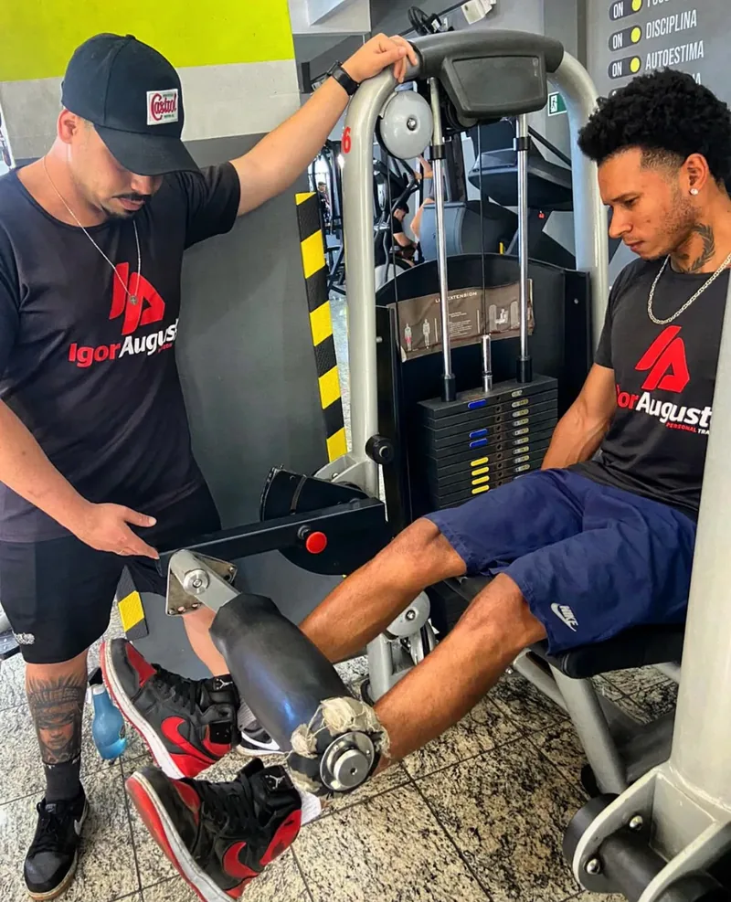 Igor ajustando a cadeira extensora para um aluno durante o treino