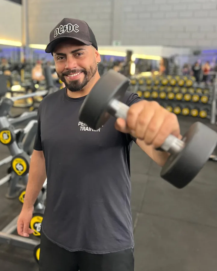 Igor sorrindo na academia, segurando um halter com o braço estendido